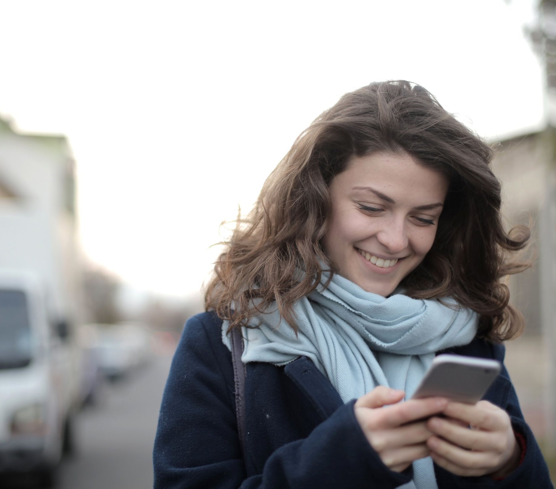 A woman smiling as she reads something on her phone in the street.